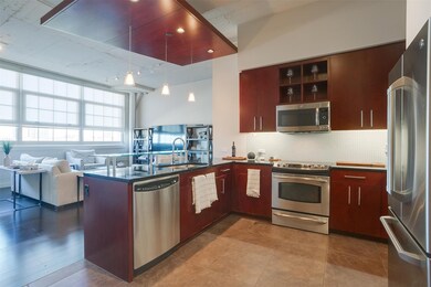 Kitchen with dark countertops, stainless steel appliances, a peninsula, hanging light fixtures, and tasteful backsplash