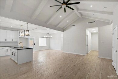 Kitchen featuring decorative light fixtures, white cabinetry, ceiling fan with notable chandelier, and an island with sink