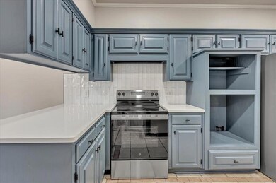 Kitchen with stainless steel appliances, light countertops, tasteful backsplash, crown molding, and light tile patterned floors