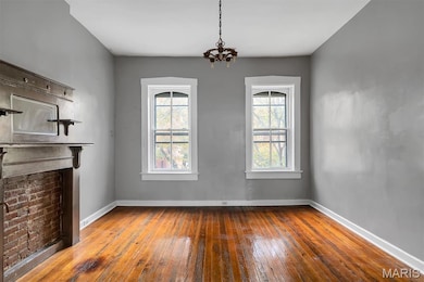 Unfurnished dining area with hardwood / wood-style floors, plenty of natural light, a fireplace, and a chandelier