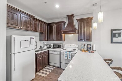 Kitchen featuring light wood-type flooring, white appliances, premium range hood, pendant lighting, and tasteful backsplash