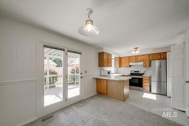 Kitchen with appliances with stainless steel finishes, under cabinet range hood, brown cabinetry, a peninsula, and light countertops