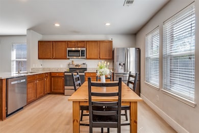 Kitchen featuring brown cabinets, appliances with stainless steel finishes, light wood-type flooring, light stone countertops, and recessed lighting