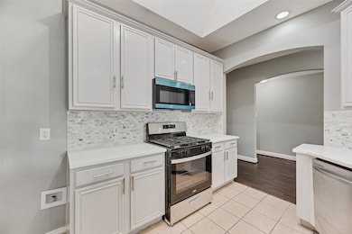 Kitchen with light tile patterned floors, appliances with stainless steel finishes, backsplash, and white cabinetry