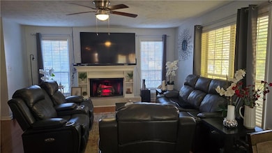 Living room featuring a fireplace with raised hearth, healthy amount of natural light, wood finished floors, ceiling fan, and a textured ceiling