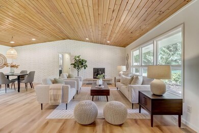 Sun-filled living room with beautiful luxury vinyl plank floors that extend throughout the main level, views of the front yard, and a new cozy wood-burning fireplace with white brick surround spanning the entire wall.
