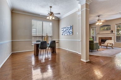 Dining room with wood-type flooring, a textured ceiling, crown molding, a ceiling fan, and a tile fireplace