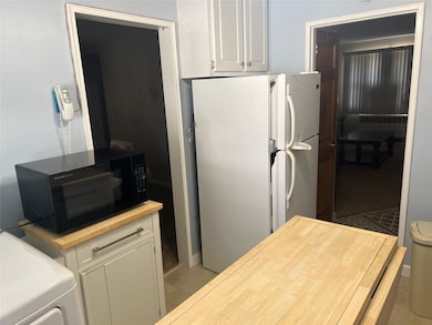 Kitchen with white cabinets, black microwave, butcher block countertops, radiator heating unit, and freestanding refrigerator