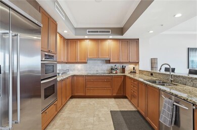 Kitchen with ornamental molding, appliances with stainless steel finishes, light stone countertops, brown cabinetry, and recessed lighting