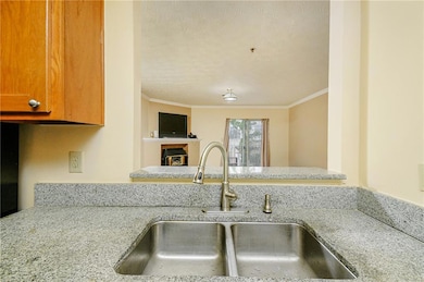 Kitchen featuring a fireplace, ornamental molding, light stone countertops, a textured ceiling, and brown cabinetry