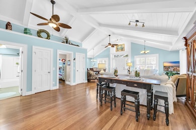 Dining space featuring a ceiling fan, high vaulted ceiling, beam ceiling, light wood-style floors, and a chandelier