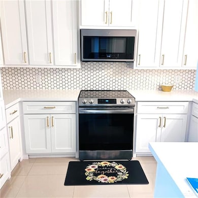 Kitchen with stainless steel appliances, light countertops, white cabinets, and backsplash