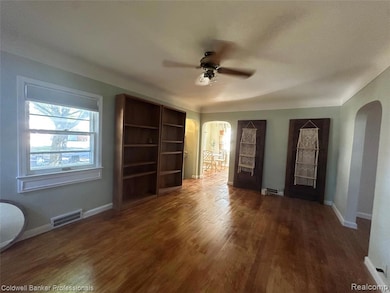 Unfurnished living room with arched walkways, dark wood-style flooring, and ceiling fan