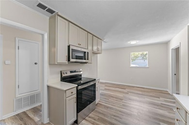 Kitchen featuring appliances with stainless steel finishes, light wood-style floors, a textured ceiling, and light stone countertops