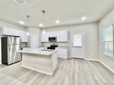 Kitchen featuring dining area appliances with stainless steel finishes, white cabinetry, light wood-style flooring, light stone counters, and a kitchen island with sink