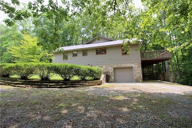 View of front facade featuring driveway, stone siding, an attached garage, and a wooden deck