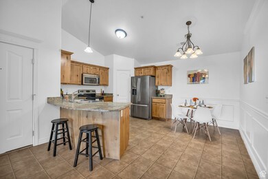 Kitchen with appliances with stainless steel finishes, a peninsula, vaulted ceiling, brown cabinets, and a kitchen bar