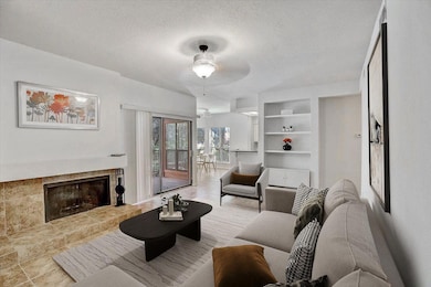 Living room featuring a fireplace with raised hearth, a textured ceiling, built in shelves, tile patterned floors, and ceiling fan