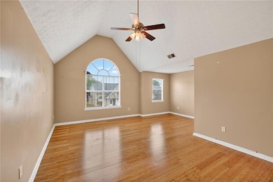 Spare room featuring vaulted ceiling, light wood-type flooring, ceiling fan, and a textured ceiling