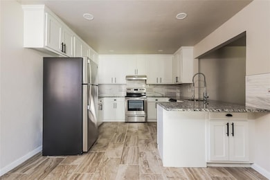 Kitchen with stainless steel appliances, dark stone counters, a peninsula, backsplash, and white cabinetry