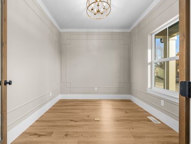 Unfurnished room with light wood-type flooring, crown molding, a chandelier, and a decorative wall