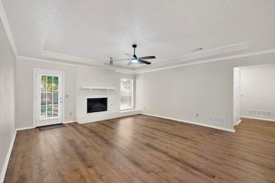 Unfurnished living room with a raised ceiling, dark wood-style flooring, a brick fireplace, ceiling fan, and attic access