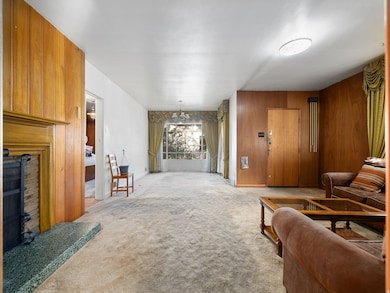 Living room featuring light carpet, wooden walls, a fireplace, and a chandelier