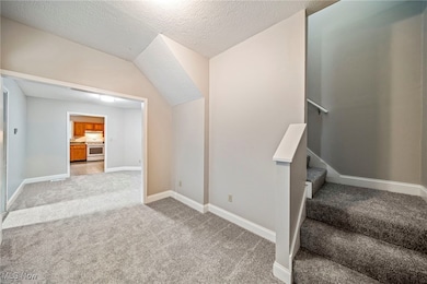 Stairway with carpet, a textured ceiling, and lofted ceiling
