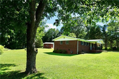 View of home's exterior with crawl space, a yard, brick siding, a porch, and view of wooded area