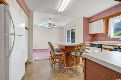 Kitchen featuring white appliances, light countertops, ceiling fan, a kitchen bar, and white cabinetry