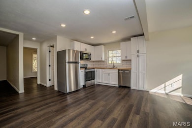 Kitchen featuring appliances with stainless steel finishes, white cabinets, backsplash, dark wood-style flooring, and recessed lighting