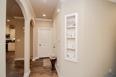 Hallway with arched walkways, ornamental molding, built in features, dark wood-style flooring, and recessed lighting