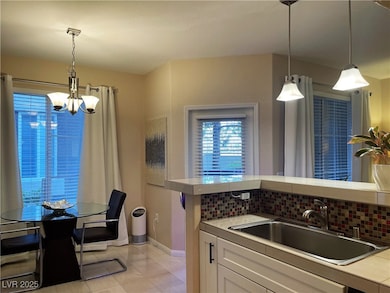 Kitchen featuring white cabinetry, pendant lighting, decorative backsplash, a chandelier, and light tile patterned floors