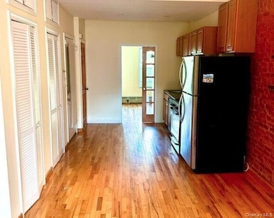 Kitchen featuring stainless steel appliances, brown cabinetry, brick wall, light wood-type flooring, and baseboard heating