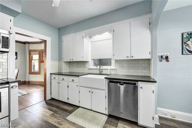 Kitchen featuring backsplash with farmhouse sink, dark hardwood / wood-style floors, appliances with stainless steel finishes, and white cabinetry.
