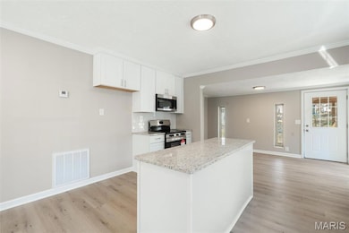 Kitchen featuring a kitchen island, light wood finished floors, white cabinetry, appliances with stainless steel finishes, and visible vents