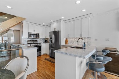 Kitchen with stainless steel appliances, a peninsula, light wood-style floors, white cabinetry, and recessed lighting