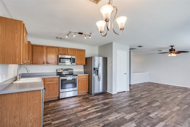 Kitchen with pendant lighting, appliances with stainless steel finishes, brown cabinetry, light countertops, and dark wood finished floors