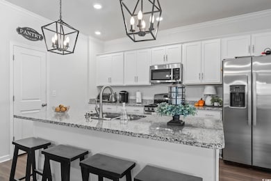 Kitchen featuring stainless steel appliances, dark wood finished floors, an island with sink, white cabinets, and crown molding