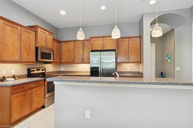 Kitchen featuring stainless steel appliances, arched walkways, brown cabinets, decorative light fixtures, and light tile patterned flooring
