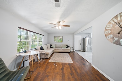 Bright and welcoming living room with hardwood floors, large windows, and a ceiling fan for comfort.