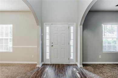 Entrance foyer featuring baseboards, dark colored carpet, arched walkways, and dark wood-type flooring