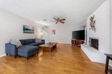 Living area with a textured ceiling, light wood-style floors, a fireplace, and a ceiling fan