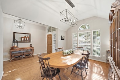 An elegant formal dining room with soaring ceilings, a modern linear chandelier, and rich wood flooring, perfect for holiday gatherings and special meals.
