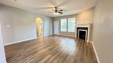 Unfurnished living room with arched walkways, wood finished floors, a fireplace, and ceiling fan