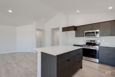 Kitchen with appliances with stainless steel finishes, light wood finished floors, a kitchen island, recessed lighting, and dark brown cabinets