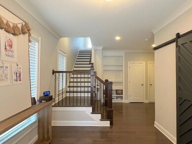 Staircase with a barn door, wood finished floors, ornamental molding, baseboards, and recessed lighting
