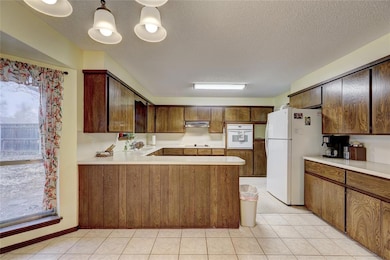 Kitchen featuring white appliances, under cabinet range hood, healthy amount of natural light, a peninsula, and a textured ceiling