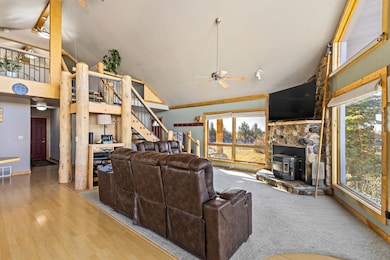 Living room featuring high vaulted ceiling, a wood stove, a ceiling fan, stairs, and wood finished floors