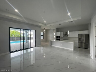 Kitchen with light tile patterned floors, a tray ceiling, an island with sink, stainless steel appliances, and pendant lighting